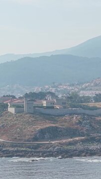A vertical 9:16 video clip showcasing the historic Castelo de Monterreal perched on a rocky hilltop overlooking the Atlantic Ocean in Baiona, Galicia, Spain.