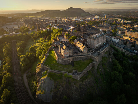 Aerial view of Edinburgh Castle perched on its volcanic rock, surrounded by lush green trees and the historic cityscape of Edinburgh, Scotland, United Kingdom.