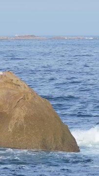 Vertical 9:16 video showing a large rocky formation emerging from the Atlantic Ocean near Baiona, Spain. No people are visible, emphasizing the natural, coastal scenery.