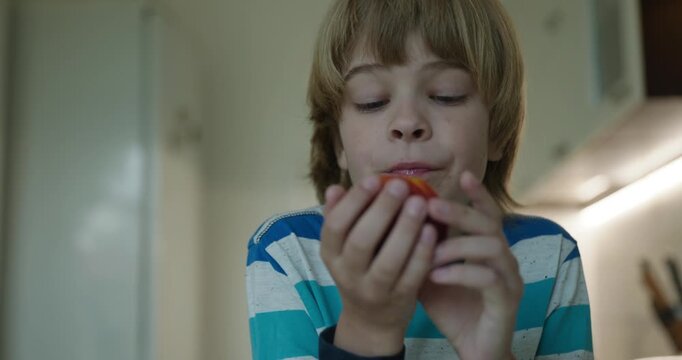 Caucasian kid boy enjoy eating peach in kitchen. 4K 10-bit