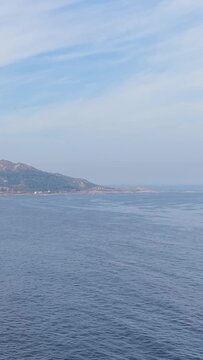 Vertical 9:16 video showing a wide view of the coastline near Baiona, Spain. The sky is partly cloudy with soft, natural daylight.