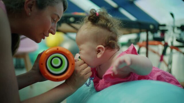 Baby exercising upper body strength on a therapy ball, receiving physical therapy and developmental assistance from an adult