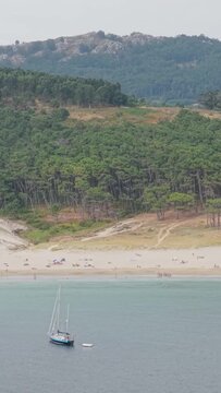 Vertical 9:16 aerial video showcasing Praia de Melide in Cangas, Spain. Rolling hills and rocky terrain rise in the background, highlighting the natural beauty of this Galician coastal landscape.