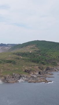 Vertical 9:16 aerial video showing the rugged rocky coastline and green hills of Praia de Melide, near Cangas, Spain. Filmed in a vertical format.