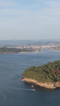 Vertical 9:16 aerial video of Illa de Tambo, a lush green island off the coast of Combarro, Spain. Captured in vertical format.