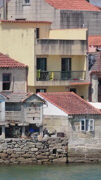 Vertical 9:16 video crop showing a close-up of traditional stone waterfront houses with red-tiled roofs in Combarro, Spain.