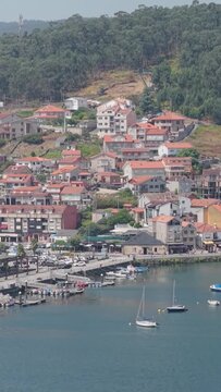 A vertical 9:16 aerial shot captures the picturesque marina and hillside village of Combarro, Spain.