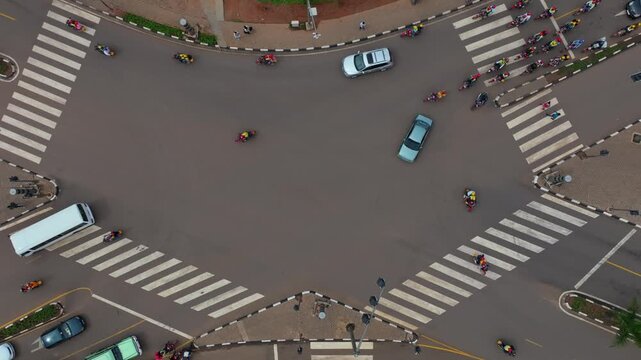 Aerial view of traffic with cars, motorcycles, and a bus navigating a roundabout with crosswalks in Kigali, Kigali City, Rwanda.