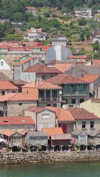Vertical 9:16 video showing a close view of the iconic waterfront houses and stone granaries (horreos) with red-tiled roofs in Combarro, Galicia, Spain.