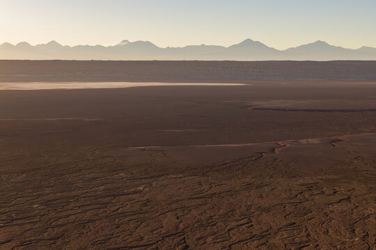 Aerial view of Atacama Desert with its vast arid landscape, salt flats, and distant mountain range under a soft golden light, Chile.