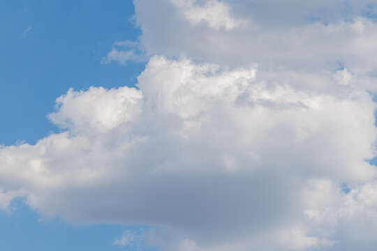 Clouds form shapes in a blue sky during the day over a sunny landscape