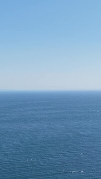Vertical format video showing a clear, unobstructed view of the Atlantic Ocean horizon under a bright blue sky, filmed at Faro de Fisterra in Finisterre, Galicia, Spain.