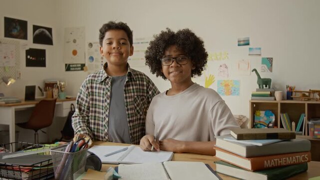 Portrait of two African American boys smiling at camera while sitting at desk with schoolbooks. Perfect for educational marketing, tutoring services, and e-learning advertisements