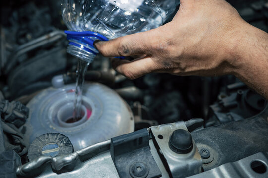 Mechanic pouring antifreeze into car coolant tank during engine service, repair and maintenance.