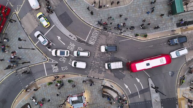 High-angle drone shot of busy London intersection with cars, vans, red bus, and pedestrians. Urban traffic flow and city life from above.