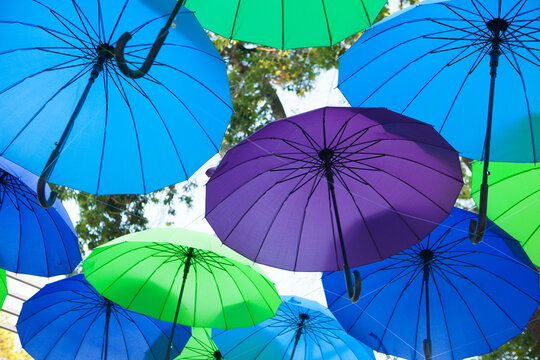 Blue, green, and purple umbrellas hang against a bright sky, minimalist outdoor decoration, creative festival background.