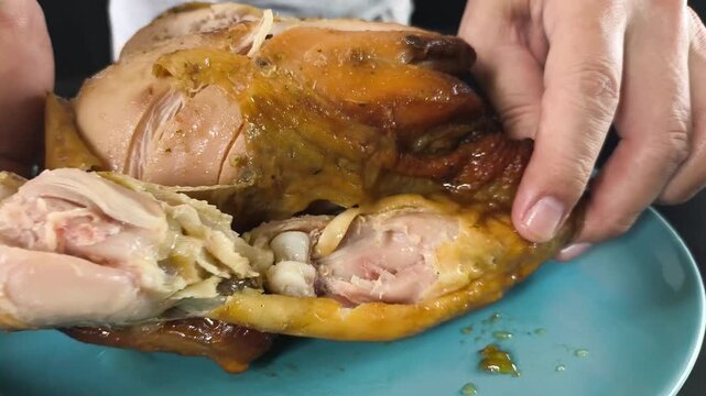 Pulling apart a tender baked chicken leg, showcasing the juicy meat texture and crispy skin during food preparation.