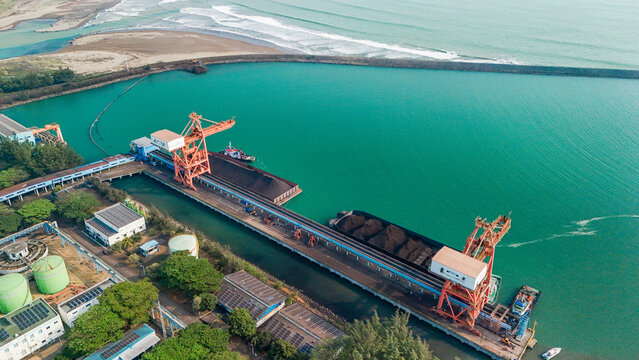 Aerial view of a coal terminal with large orange cranes loading barges in a coastal port facility