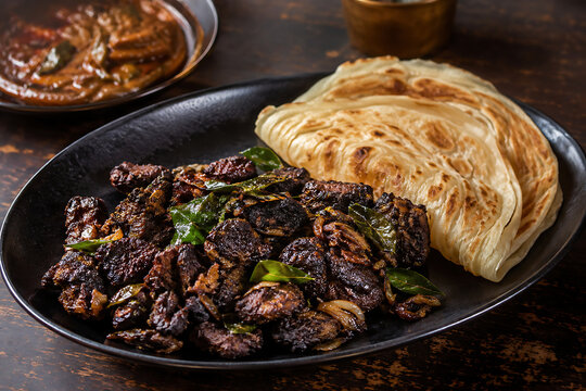 Traditional Kerala beef fry with caramelized onions, curry leaves and black pepper, served with parotta, authentic local restaurant presentation