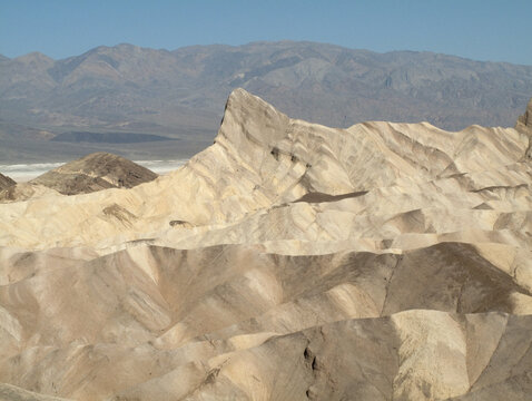 View of the golden, eroded badlands and sharp ridges of Zabriskie Point under a clear sky in Death Valley, California, United States.