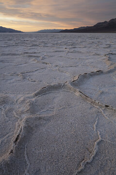View of Badwater Basin salt flats with hexagonal salt crust patterns under a soft sunrise sky in Death Valley, California, United States.