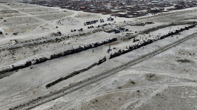 Aerial view of the historic Uyuni Train Cemetery featuring rusted steam locomotives and abandoned train carriages scattered across the arid desert landscape in Uyuni, Potosi Department, Bolivia.