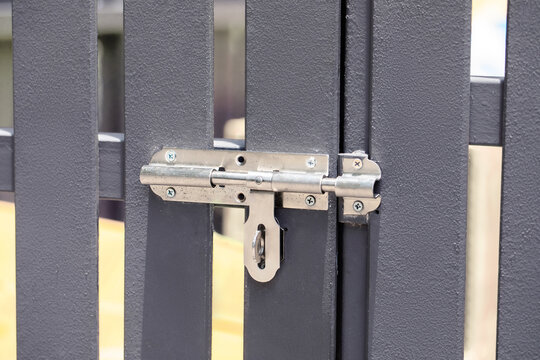 Close-up of metal gate latch and lock mechanism on gray fence panel, security hardware detail concept
