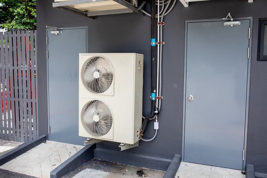 Air conditioning condenser units mounted on gray exterior wall of building with electrical wiring and doorway, HVAC infrastructure concept