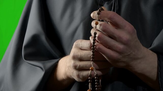 Monk slowly counting wooden prayer beads in close-up against green background