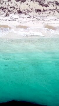 Vertical aerial view of turquoise sea and white sand along the Sardinian coast showing crystal clear water, shoreline and Mediterranean beach scenery.