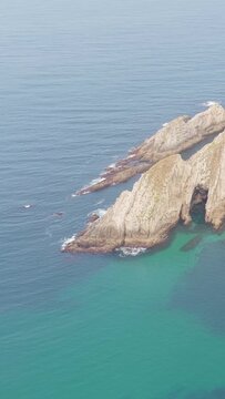 Vertical 9:16 aerial video showing the rugged rocky coastline and turquoise waters at El Peine del Mar near Cudillero, Asturias, Spain.