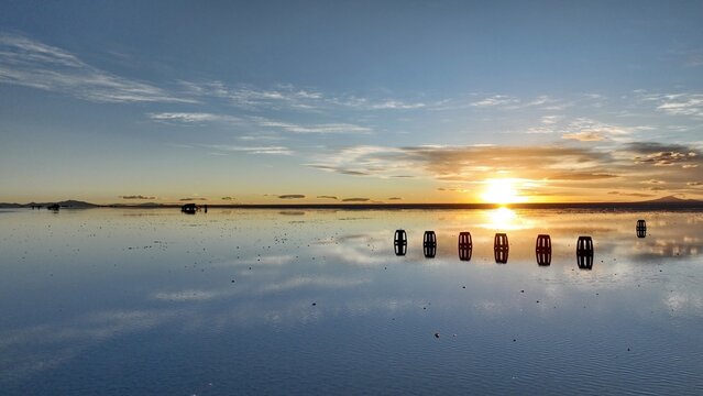 Aerial view of the Uyuni Salt Flat at sunset, with the golden sun reflecting on the mirror-like surface of the water, creating a serene landscape in Uyuni, Potosi Department, Bolivia.