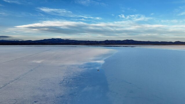 Aerial view of Uyuni Salt Flat with its vast white salt crust reflecting the blue sky and distant mountains under soft light in Uyuni, Potosi Department, Bolivia.