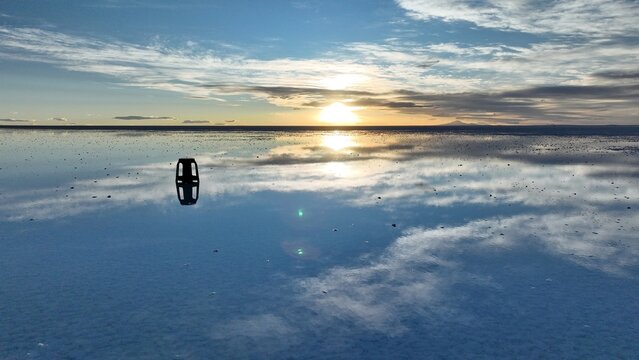 Aerial view of Uyuni Salt Flat at sunset with a reflective water surface creating a mirror effect and a small stool placed on the salt crust in Uyuni, Potosi Department, Bolivia.