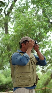 Happy senior man walking through a forest while taking photos of nature. Active aging, retirement lifestyle creative hobby, healthy longevity. Life insurance and fulfilling life after retirement.
