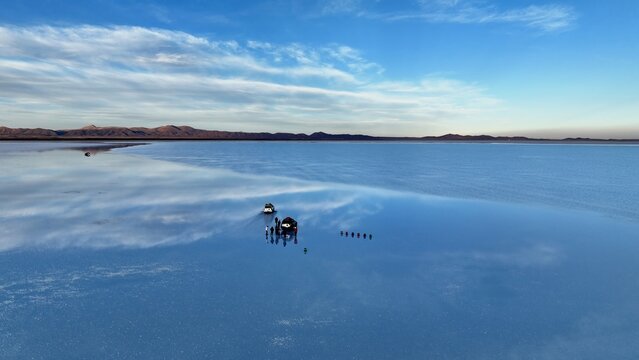 Aerial view of Uyuni Salt Flat with a mirror-like reflection of the sky on the water surface, featuring SUVs and a group of people standing on the salt, Uyuni, Potosi Department, Bolivia.