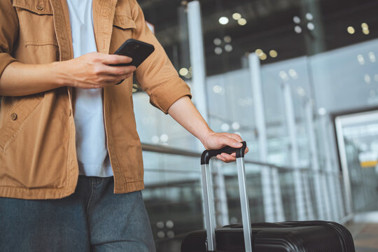 Traveler using smartphone while holding suitcase at airport terminal, mobile technology and modern travel concept