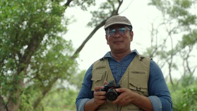 Happy senior man walking through a forest while taking photos of nature. Active aging, retirement lifestyle creative hobby, healthy longevity. Life insurance and fulfilling life after retirement.
