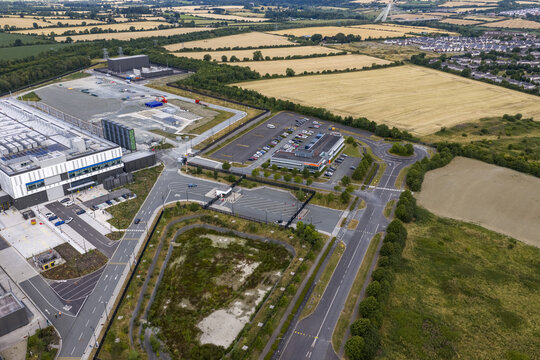 Aerial view of a modern industrial data center complex with large server buildings, parking lots, and surrounding green fields in Drogheda, County Louth, Ireland.