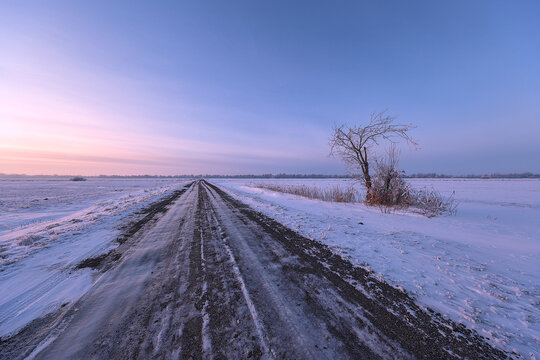 Icy Winter Road Through Snow Covered Fields at Pink and Blue Twilight