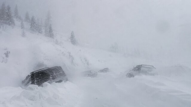 Vehicles stranded during severe blizzard with heavy snowfall and whiteout conditions on mountain road landscape