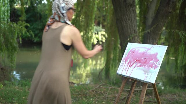 Beautiful woman artist painting on a canvas by the river in a dress
