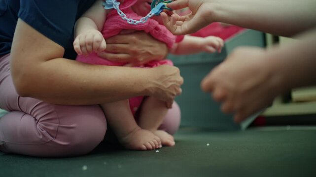 Adult hands gently offering a pacifier to a baby wearing a pink outfit, symbolizing care, comfort, and parenting