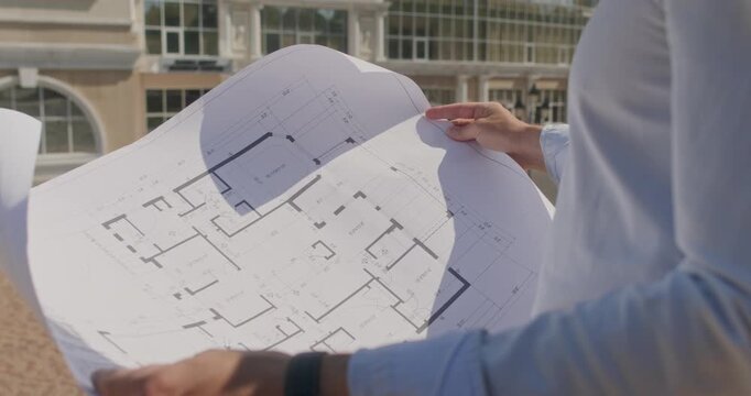 A close-up of an engineer holding a large paper drawing in front of him against the backdrop of a large shopping mall.