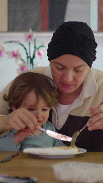 Mother sharing mealtime while holding toddler on lap at family table, intimate home moment highlighting closeness, caregiving, attachment, resilience and everyday family life