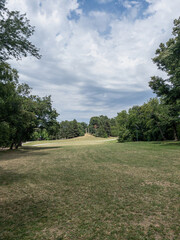 Fototapeta premium Open park field under a cloudy sky with distant trees, clear horizon, and expansive grass, a tranquil nature scene ideal for relaxation and outdoor exploration.