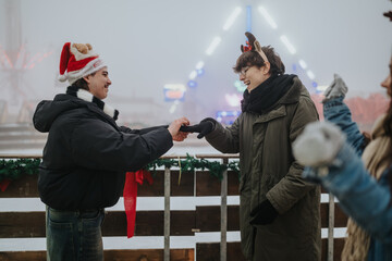 Fototapeta premium Two friends exchange a glove while smiling at a decorated outdoor winter market. They share a playful moment amid holiday lights and seasonal decorations.