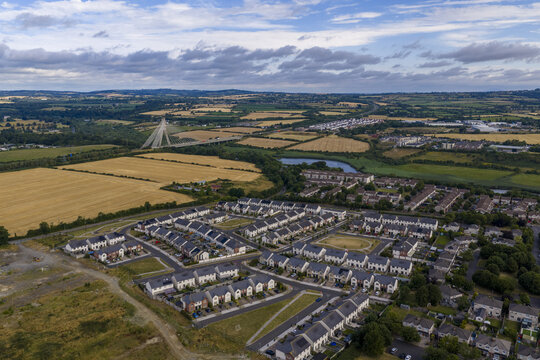 Aerial view of a modern residential housing development surrounded by golden fields, with the Mary McAleese Boyne Valley Bridge in the distance in Drogheda, County Louth, Ireland.