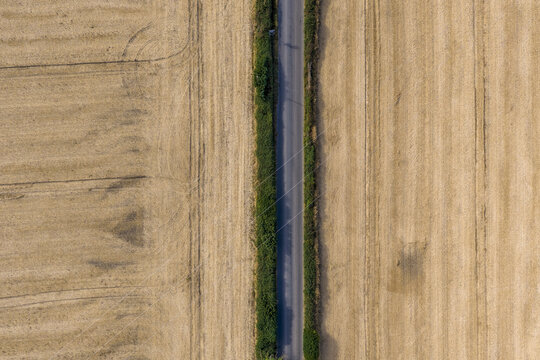 Aerial view of a straight rural road flanked by green hedges and surrounded by golden harvested wheat fields in Drogheda, County Louth, Ireland.