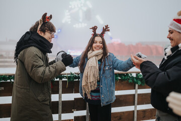 Fototapeta premium Three friends wearing reindeer antlers and winter coats share a joyful moment outdoors. A festive group enjoys holiday cheer together at an outdoor ice rink railing.